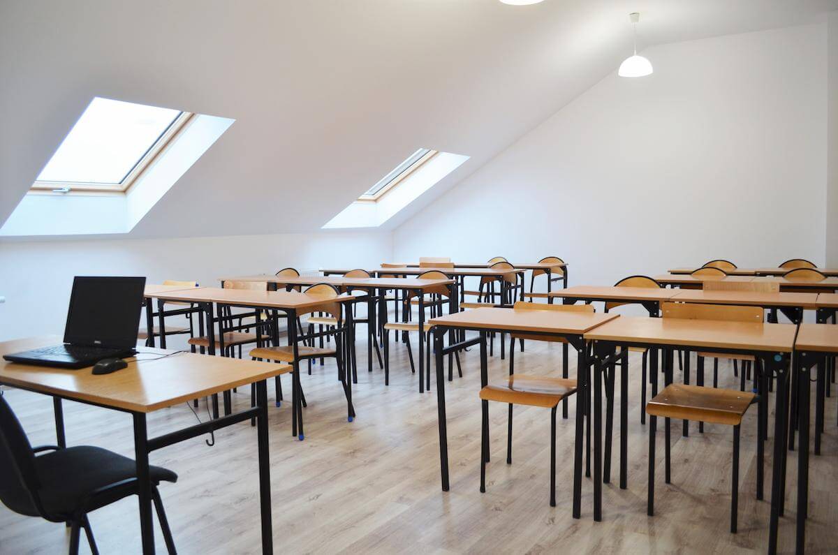 sala szkoleniowa z ławkami w układzie szkolnym, na pierwszym planie biurko z laptopem